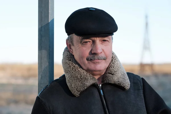 Un homme âgé avec une moustache porte une casquette et une veste chaude dans la rue — Photo