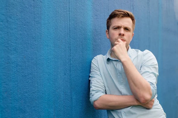 Retrato de un joven inteligente y serio de pie sobre fondo azul —  Fotos de Stock