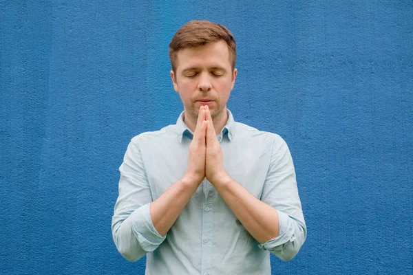 Uomo in camicia blu che medita o prega Dio, palme insieme al petto — Foto Stock