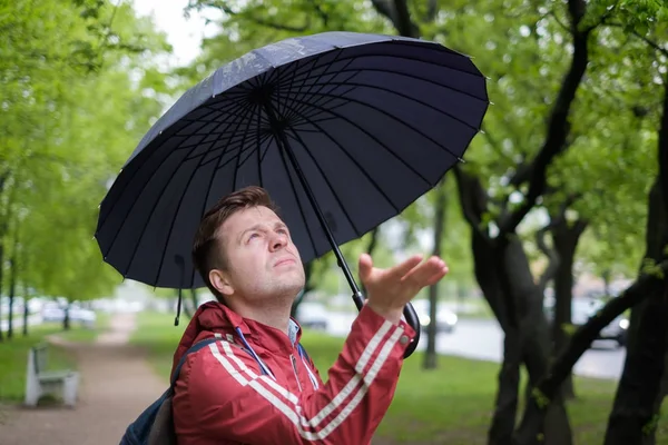 Deszczowy dzień - młodego mężczyznę idącego z niebieski parasol, sprawdzanie deszcz — Zdjęcie stockowe