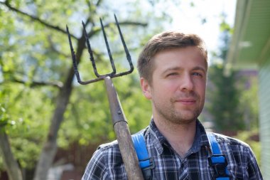 Yaz gününde dirgen ile ayakta beyaz yakışıklı olgun adam portresi