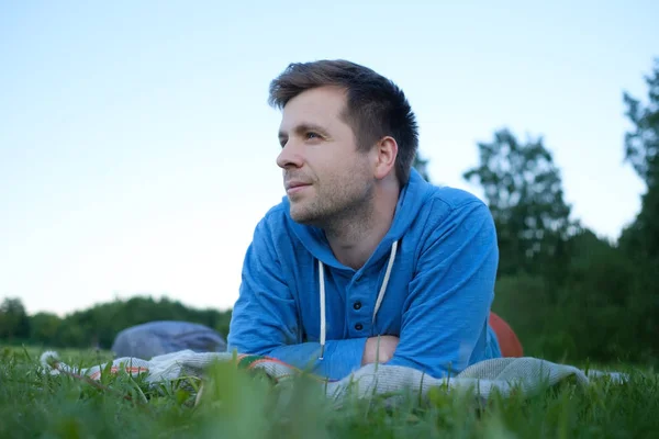 Gelukkig Kaukasische man liggen op het groene gras met uitgestrekte armen. — Stockfoto