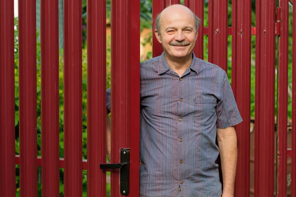 Um homem idoso encontra convidados em uma cerca de metal vermelho . — Fotografia de Stock