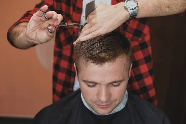 Kaukasischer junger Mann im Friseursalon. Friseur schneidet sich die Haare im Hipster-Stil. — Stockfoto