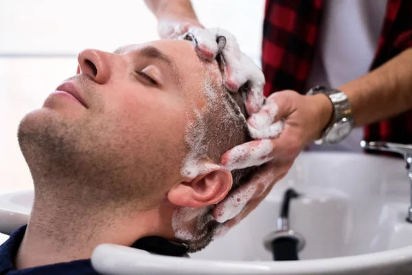 Genç Mcaucasian adam içinde Berber saç kesimi sırasında rahatlatıcı