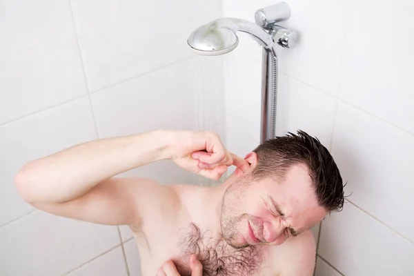 Uomo caucasico pulizia l'orecchio mentre si fa una doccia e in piedi sotto l'acqua che scorre . — Foto Stock