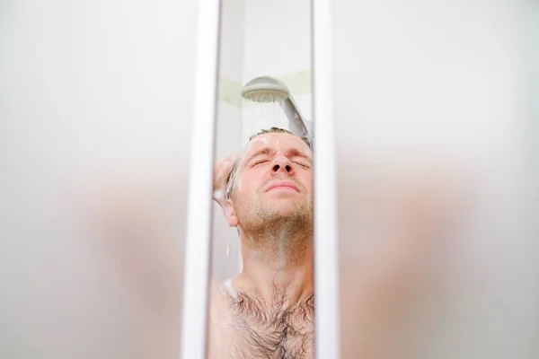 Young caucasian man washing his hair, taking a shower with foam on his head holds fingers in hair. — Stockfoto