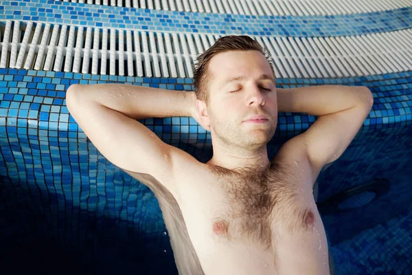 Quell'uomo sta riposando sul bordo della piscina. Le mani sono dietro la testa . — Foto Stock