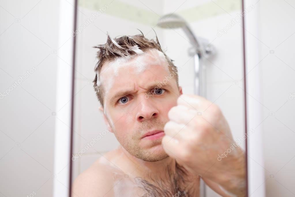 An angry man is showing a fist. He takes a shower and tries to protect his private space.