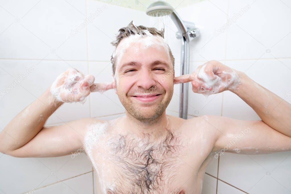Youthful hairy guy washing in bathroom. A man enjoys washing his head and ears.