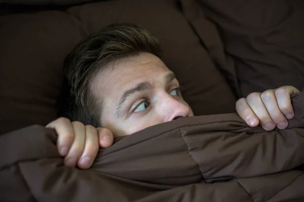 Кавказький молодий чоловік ховається в ліжку під ковдрою вдома. — стокове фото