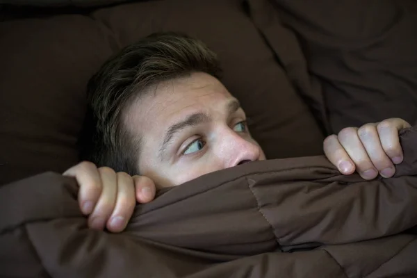 Caucásico joven escondido en la cama debajo de la manta en casa . — Foto de Stock