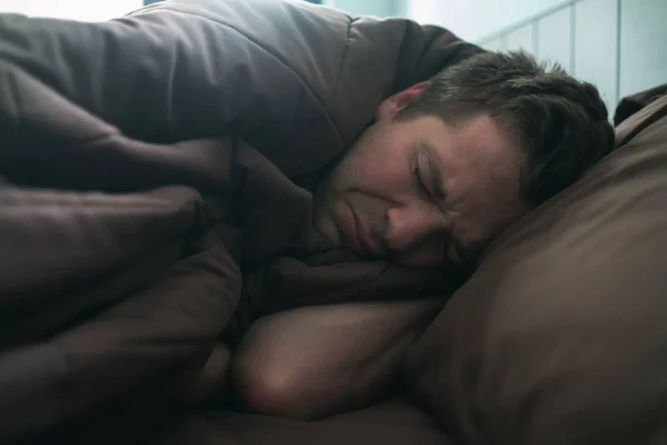 Offended caucasian man lie on bed and cover himself with blanket. He is about to cry. — Stock Photo, Image