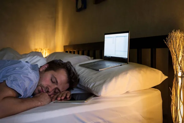 Retrato de jovem caucasiano cansado homem deitado na cama usando laptop por um longo tempo . — Fotografia de Stock