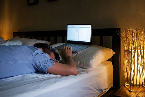 Портрет молодого кавказького втомленого чоловіка, що лежить на ліжку, використовуючи ноутбук протягом тривалого часу . — стокове фото
