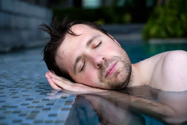 Un giovane uomo finge di dormire sul bordo della piscina, mettendo le mani sotto la testa . — Foto Stock