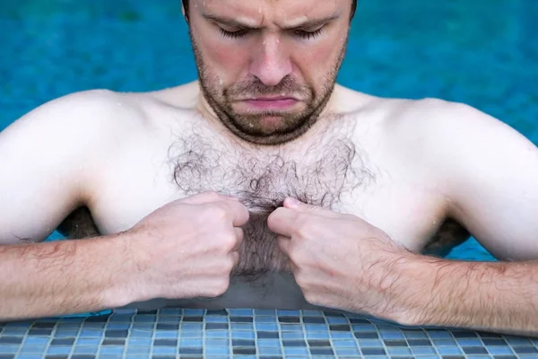 Kaukasische dude zwemmen in zwembad. Hij is op zoek op zijn haar op de borst — Stockfoto