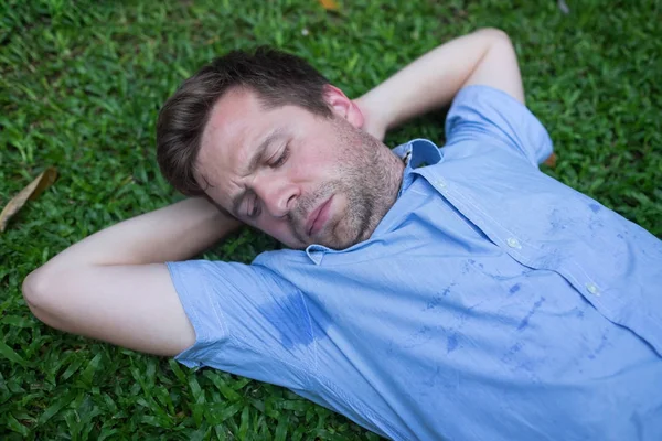 Kaukasische, jonge man is rustend op groene gras en op zoek op zijn natte shirt. — Stockfoto