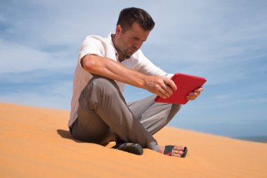Çölde kaybettim. Tablet ile kum üzerinde oturan beyaz adam. O kaybolur ve lookking içinde harita nereye gitmek