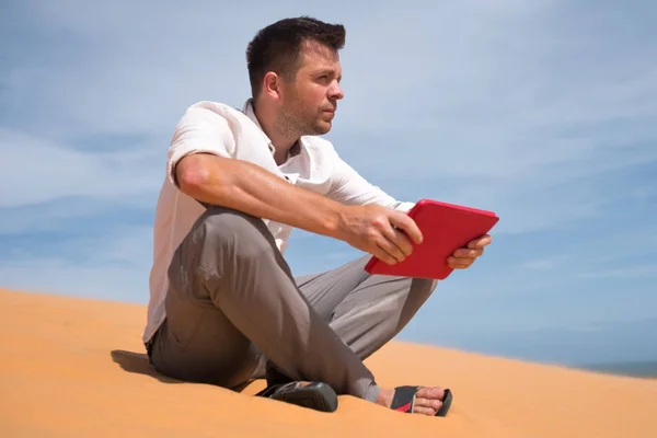 Потерялась в пустыне. Белый мужчина сидит на песке с табличкой. Он потерялся и ищет на карте, куда идти. — стоковое фото