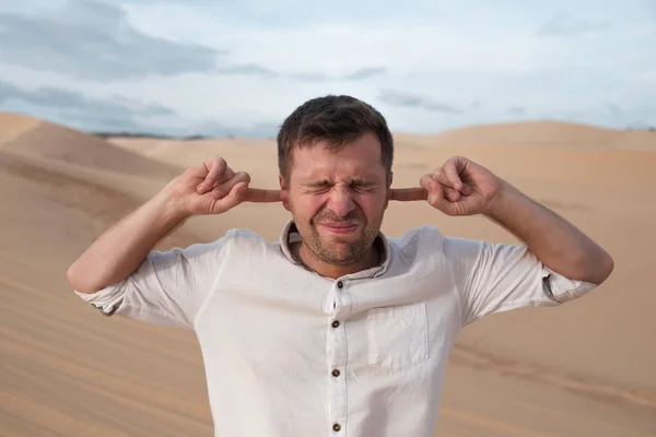 Een man van middelbare leeftijd staat alleen in de woestijn en sluit zijn oren met zijn handen. — Stockfoto