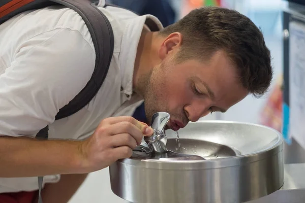 Een jongeman is drinkwater uit een gratis fontein op de luchthaven. — Stockfoto