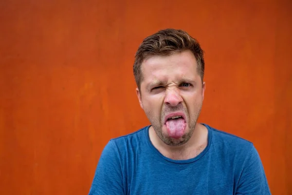 stock image A young man with a grimace of disgust on his face. He puts out his tongue.