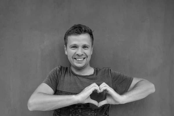 Black and white photo of caucasian man making a hand heart frame