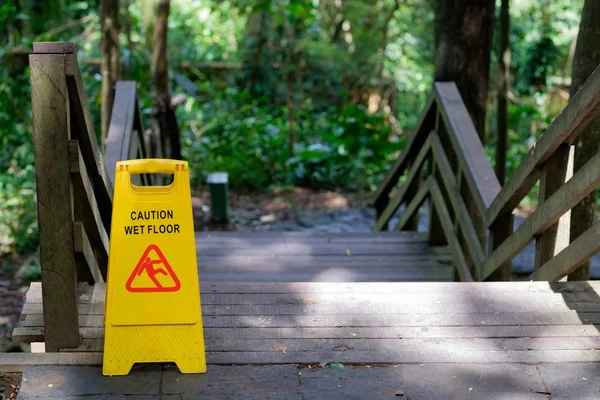 Yellow Caution slippery wet floor sign outdoors near wooden staircase