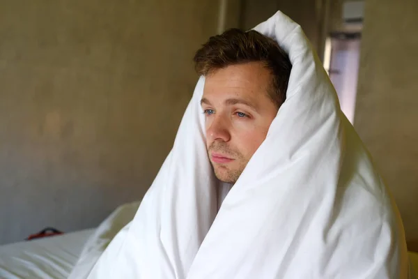 Сумний білий чоловік сидить на ліжку з головою вкритою ковдрою — стокове фото