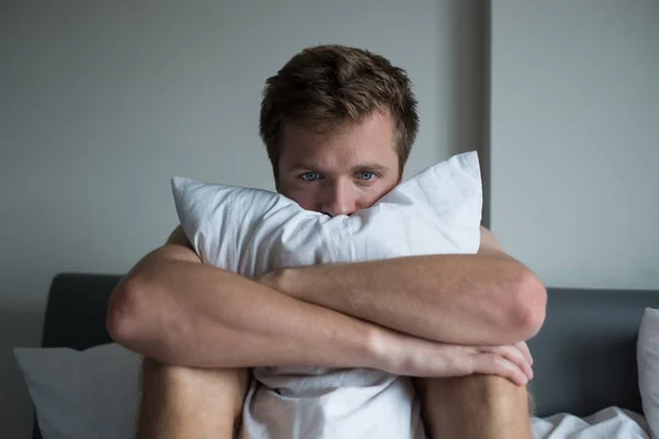 Zieke man zittend op zijn bed met zijn hoofd op zijn hand — Stockfoto