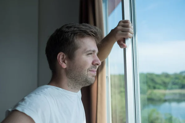 Ung man stående vid fönstret i morgon. Han står upp tidigt — Stockfoto