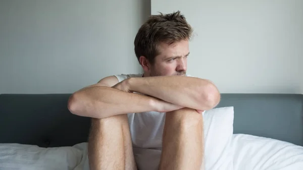 Hombre enfermo sentado en su cama con la cabeza en la mano — Foto de Stock