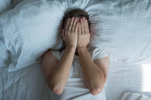 Pemuda kaukasia menutup mata dengan tangan di tempat tidur — Stok Foto