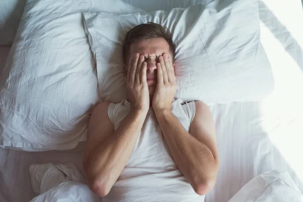 Caucasien jeune homme fermé les yeux avec les mains dans le lit — Photo