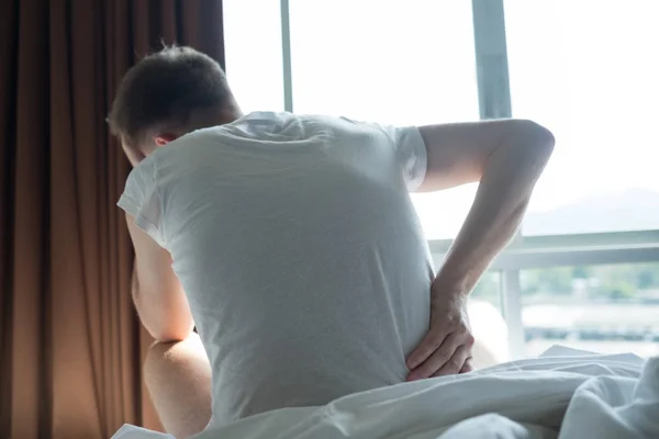 Joven sentado en el interior de la cama sintiendo dolor en la espalda — Foto de Stock