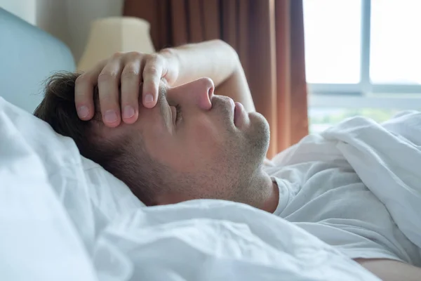 Чоловік лежить в ліжку вдома страждає від головного болю або похмілля — стокове фото