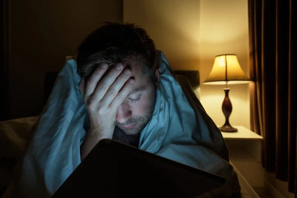 Knappe jonge man in huis lezing met tablet Pc liggend op bed's nachts. Hij is moe en wil slapen — Stockfoto