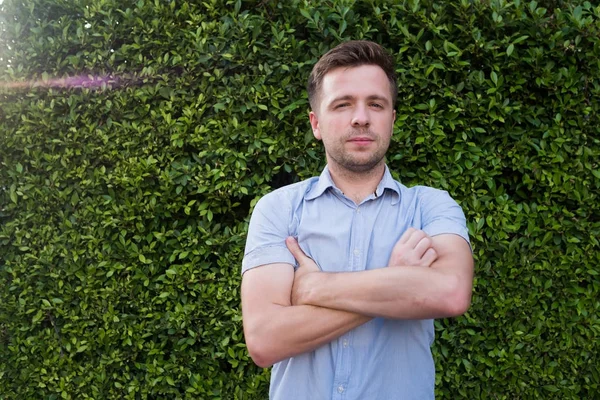 Kaukasische man in een blauw shirt reputatie in de buurt van groen gras muur. Hij is glimlachend en een gerust gevoel. — Stockfoto