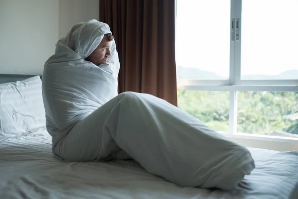 Deprimerad man som sitter på sin säng täckt med filt och titta på fönstret. Han är deprimerad efter skilsmässa — Stockfoto