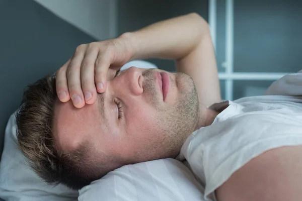 Hombre acostado en la cama en casa sufriendo de dolor de cabeza o resaca — Foto de Stock