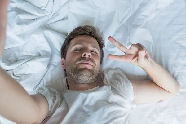 Knappe man in een wit overhemd een selfie nemen in bed — Stockfoto