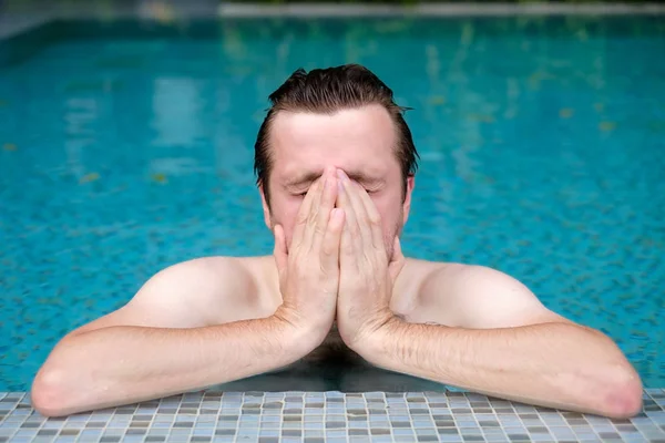 Um jovem na piscina limpa o rosto com a mão . — Fotografia de Stock