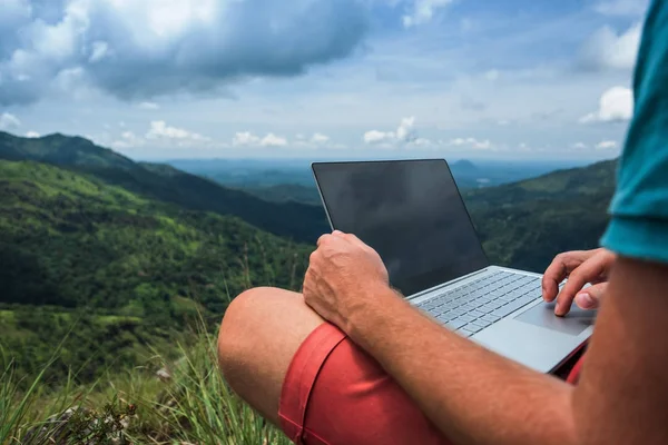 Кавказький чоловік з ноутбуком, сидячи на краю гірського Елла з приголомшливим видом на долину в Шрі-Ланці. — стокове фото