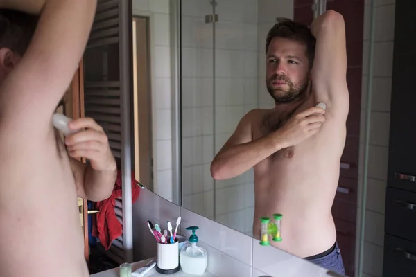 Bello uomo senza camicia che mette il deodorante in bagno — Foto Stock