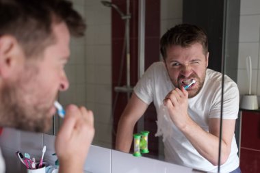 Evdeki sabah banyosunda dişlerini temizleyen adam aynaya bakıyor.