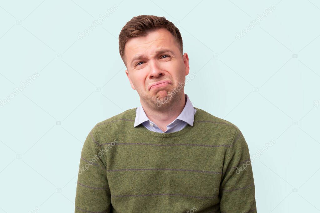 Sad and unhappy young man in green sweater looking at camera.