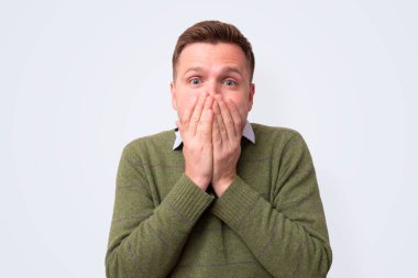 Genç beyaz adam elleriyle ağzını kapatıyor.