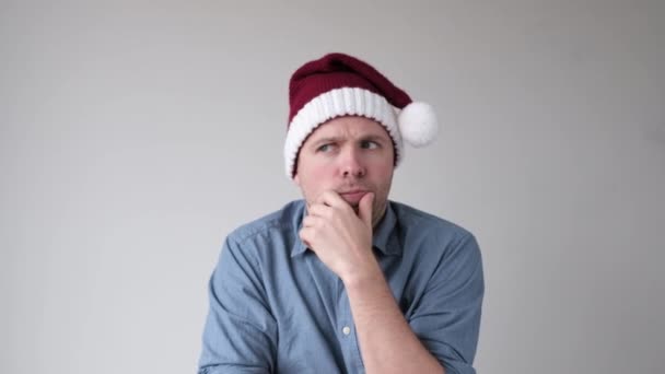 Hombre en santa claus sombrero tratando de tomar una decisión qué presentar a su familia para la Navidad . — Vídeos de Stock