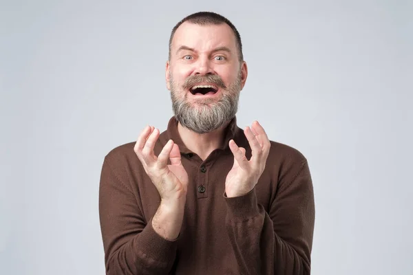 Mature scared man in brown clothes squeezes fingers from horror. — Stock Photo, Image